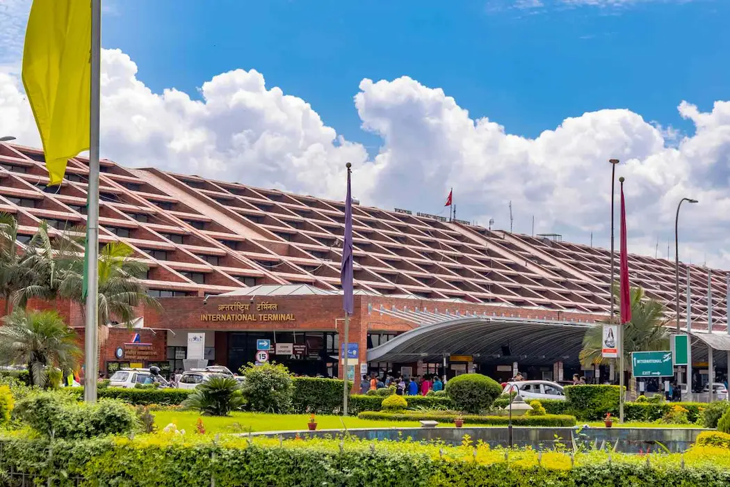 The red-brick International Terminal of Tribhuvan International Airport in Kathmandu, with its stepped roof and bilingual terminal sign, under a blue sky.